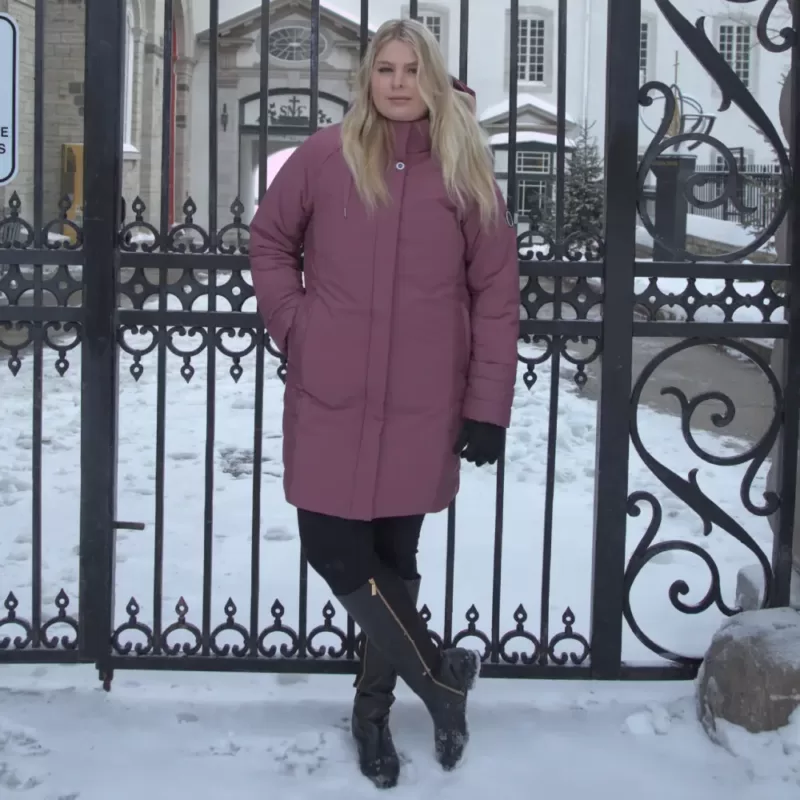 Our model wears the plus size winter jacket SIDEKICK wineberry, in front of a gate.