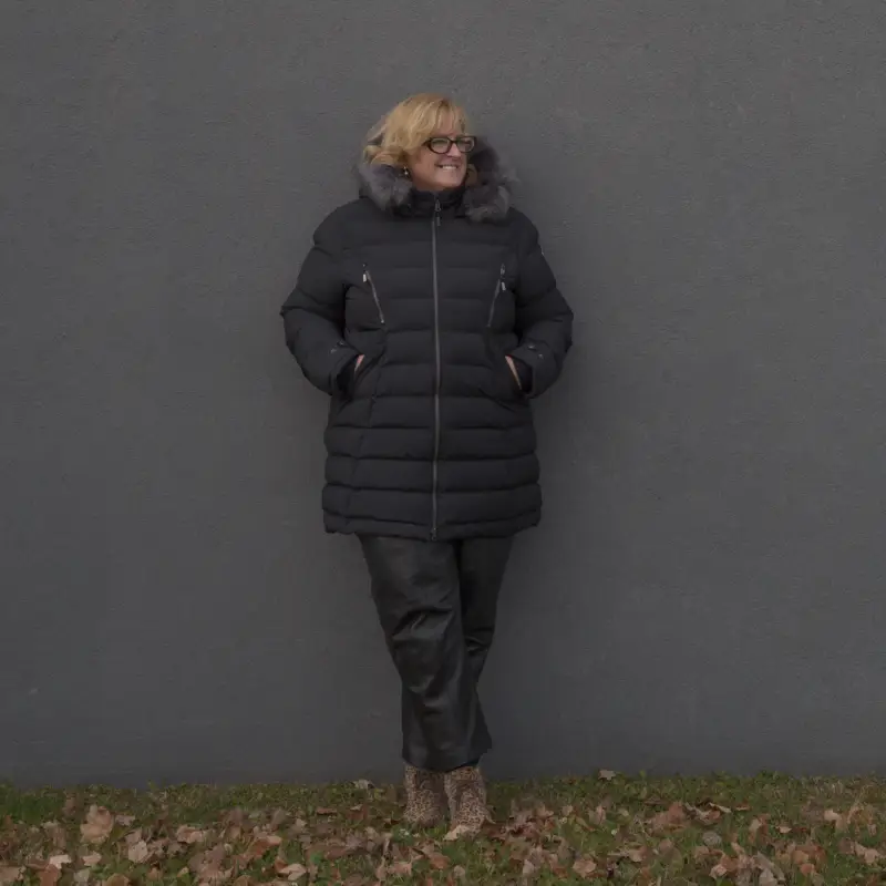 Notre modèle porte le manteau d'hiver grande taille ELEMENT noir, posant devant le mur d'un immeuble