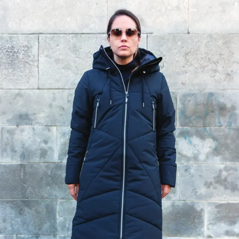 Our model wears the winter jacket long COSMO black, in front of a stone wall, 44752